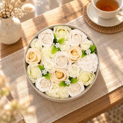 Caixa redonda de flores de sabão marfim e creme numa mesa de centro com chá