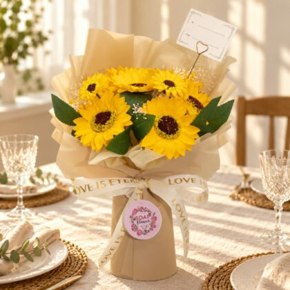 Ramo grande de girassóis de sabão com fita LOVE IS ETERNAL e etiqueta SOAP flower numa mesa posta para celebrar