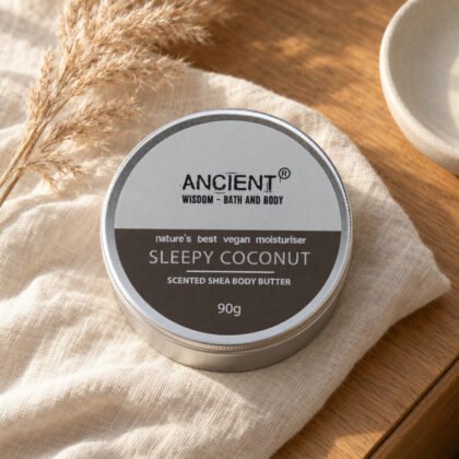 Lata de manteiga corporal Sleepy Coconut da Ancient Wisdom, 90 g, sobre linho creme numa mesa de cabeceira de carvalho