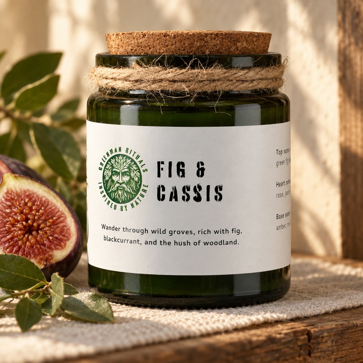 Vela Fig & Cassis da Greenman Rituals com rolha de cortiça, sobre um pano de linho numa prateleira de madeira, com figo e folhas