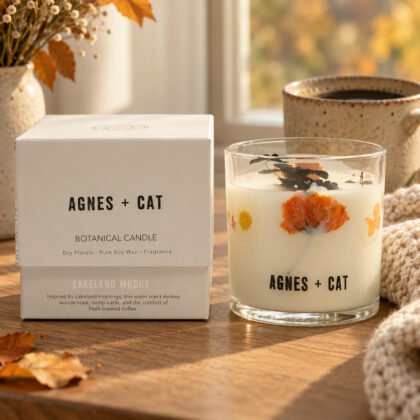 Vela botânica Agnes + Cat Lakeland Mocha com flores secas e a caixa, numa mesa de carvalho junto à janela, com uma caneca de café e uma manta de malha