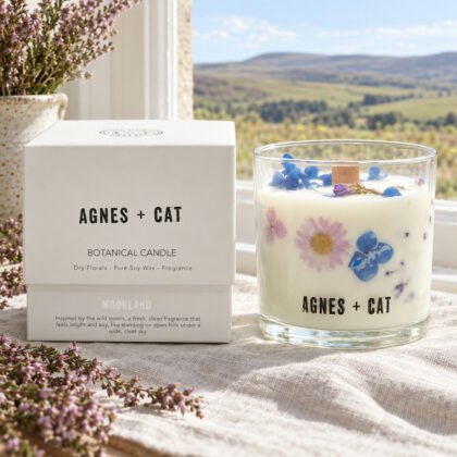 Vela botânica Agnes + Cat Moorland com flores secas e a caixa, num parapeito com linho e urze, com vista para colinas abertas