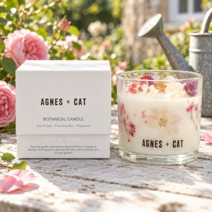 Vela botânica Agnes + Cat Roses of Sawrey com flores secas cor-de-rosa e a caixa, numa mesa de jardim com rosas