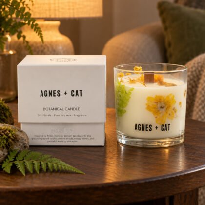 Vela botânica Agnes + Cat Rydal Oudh com flores secas e a caixa, numa mesa de carvalho escuro com musgo e fetos, à luz de um candeeiro
