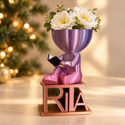 Vaso com forma de gente a ler, em rosa e violeta, sobre uma base com o nome Rita