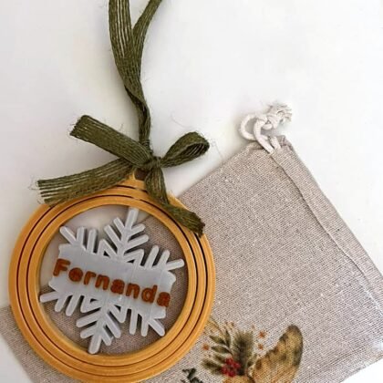 Bola de Natal personalizada com o nome Fernanda, aros dourados e floco de neve, ao lado do saco de linho Ariumô